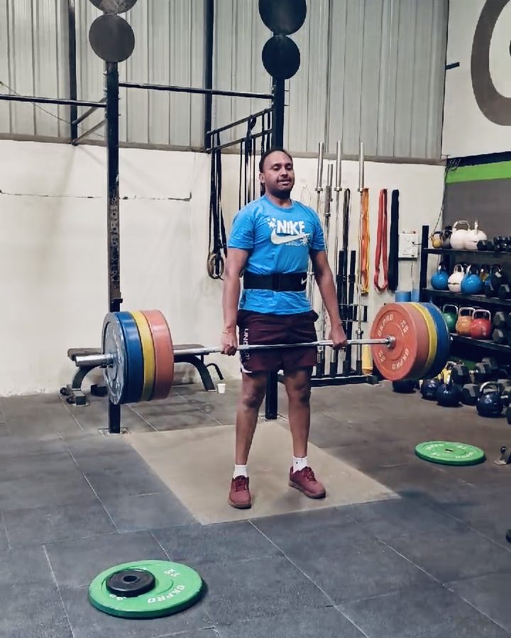 Venkat standing up with a loaded deadlift in a CrossFit gym